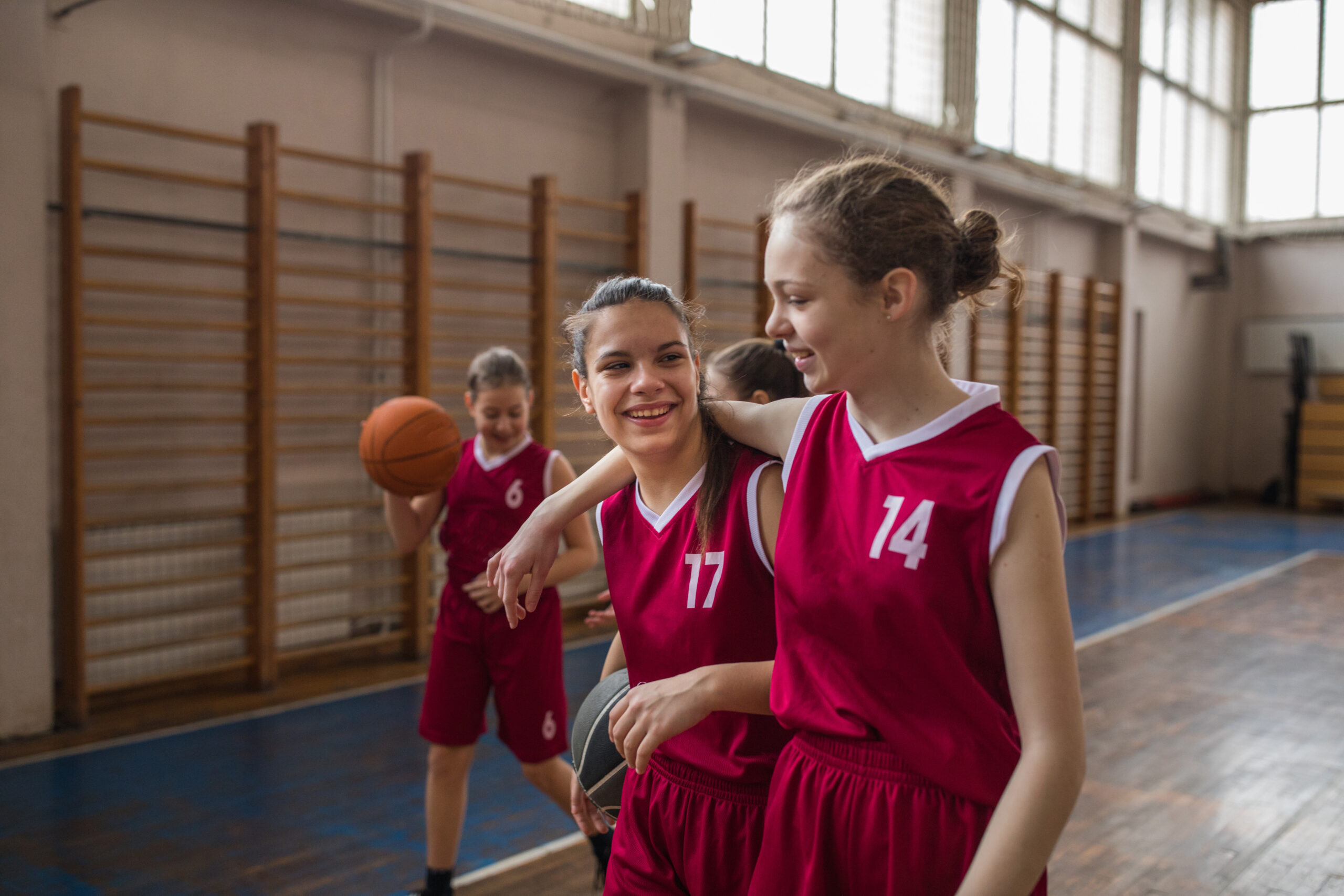 Group of girls, girls basketball players training on court indoors, hugging after match.