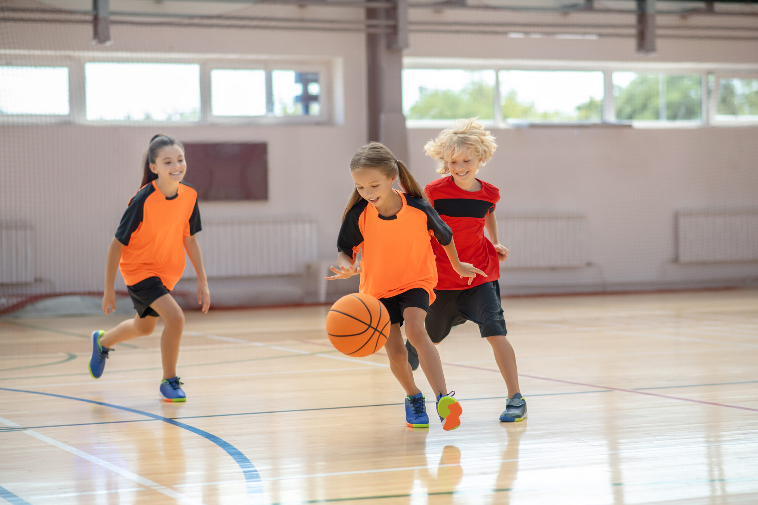 Game. Kids in bright sportswear playing basketball and running after the ball