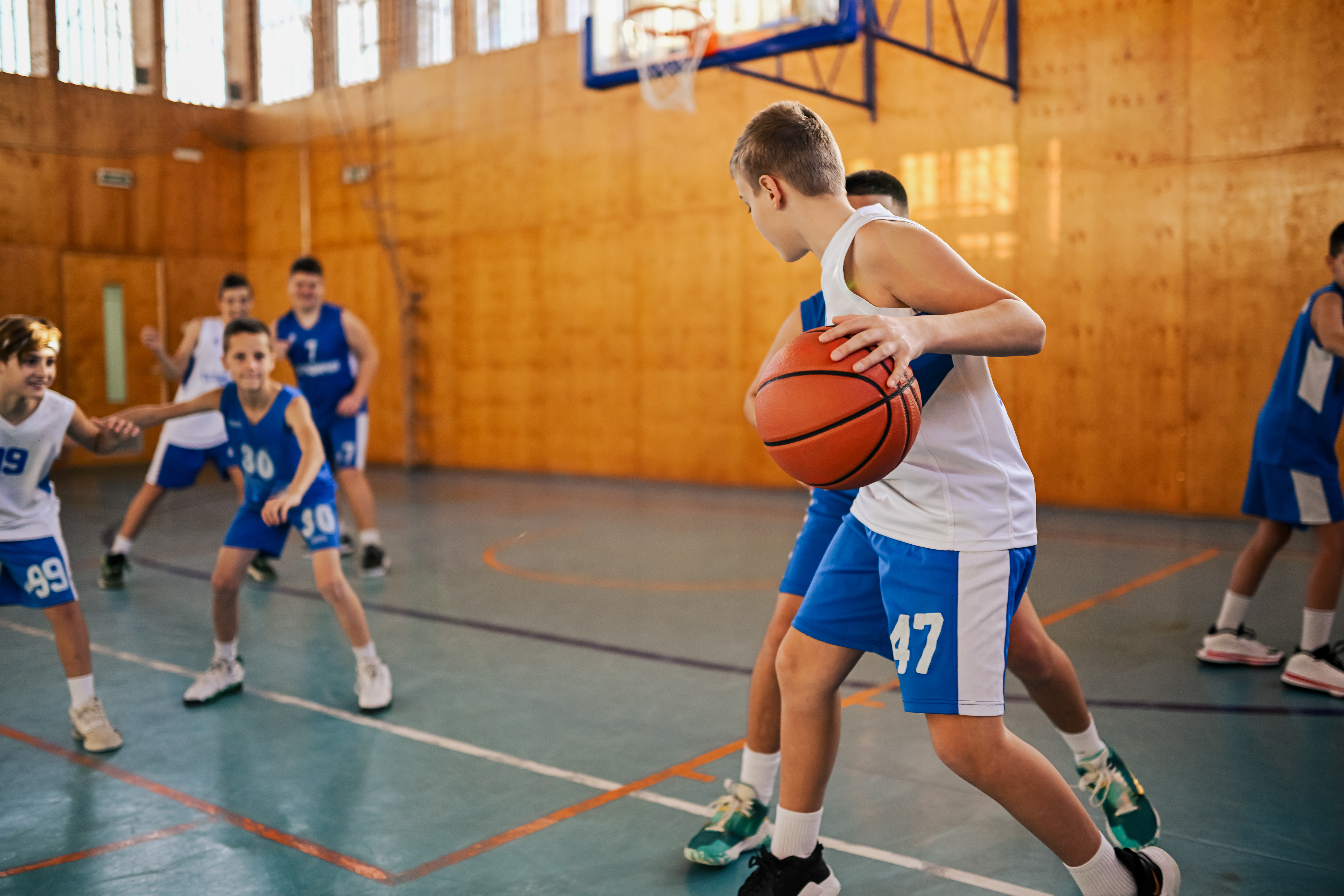 A junior basketball player is dribbling a ball while his rival is trying to steal it. A junior basketball team in action is playing basketball and practicing game during training at indoor court.